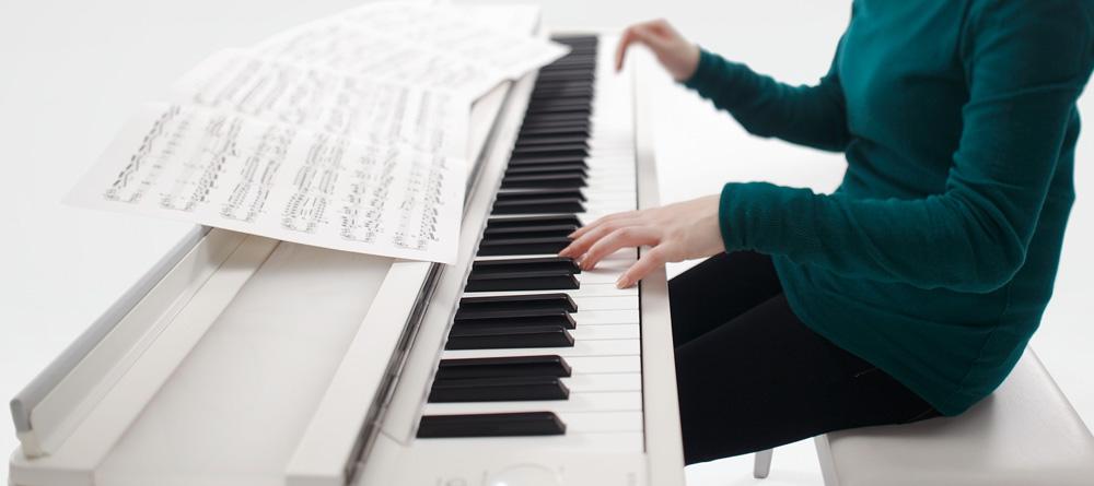 Photo of someone playing a digital piano with sheet music spread across the top of the piano