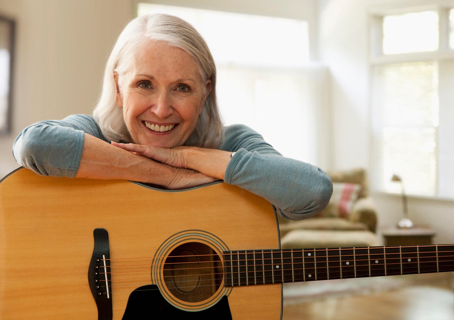 Photo of a retired couple playing acoustic guitar on a park bench