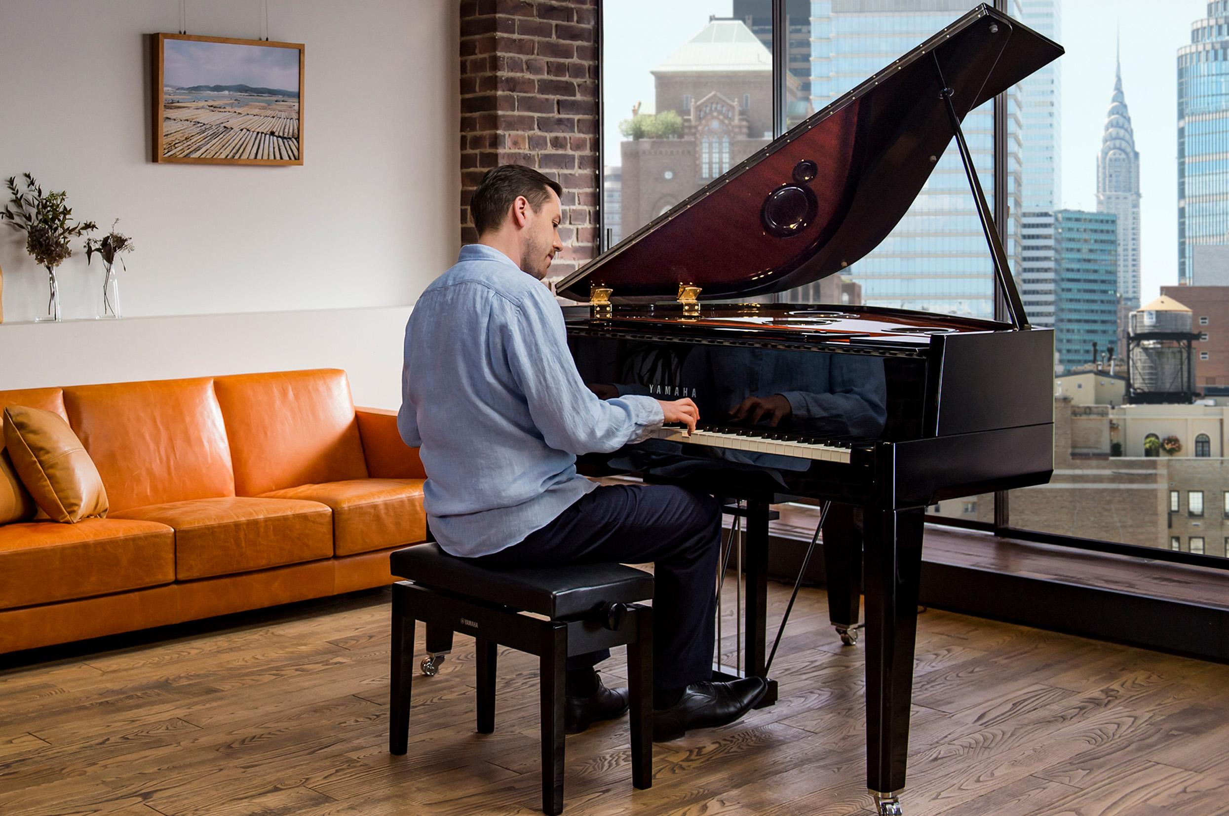 Photo of a person playing a Yamaha AvantGrand in a city apartment, with windows overlooking the cityscape