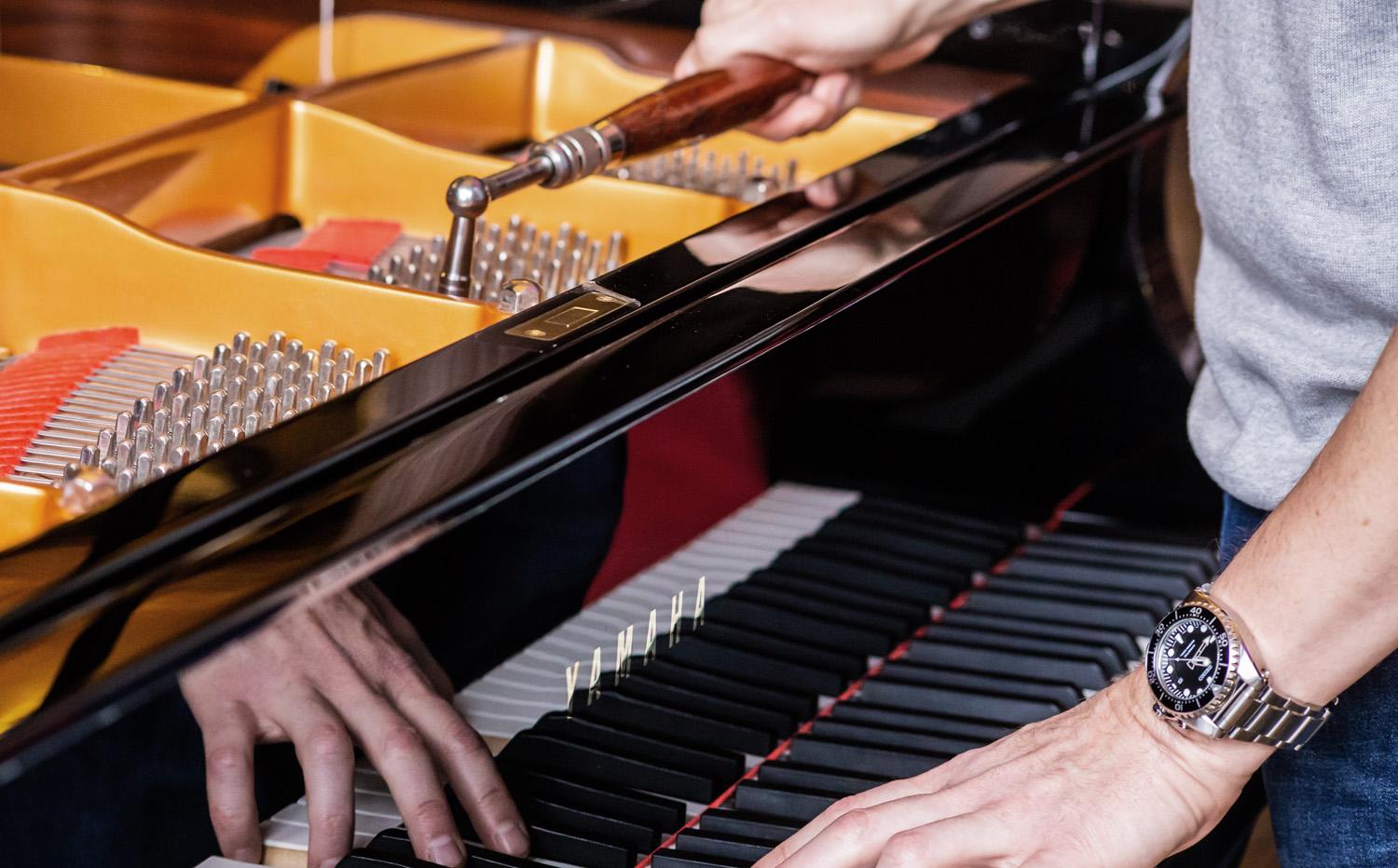 Photo of a piano tuner using a tuning hammer to tune a Yamaha grand piano