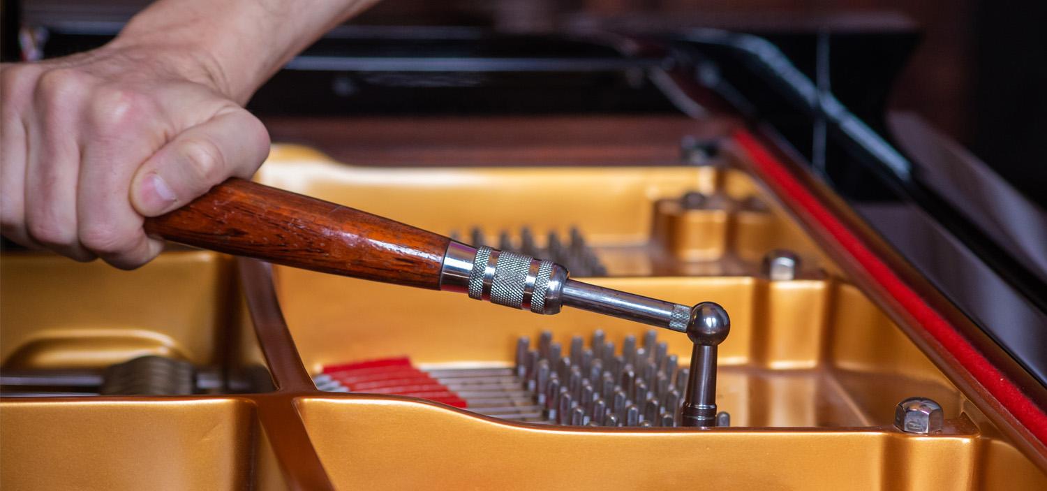 Photo of a piano tuner using a tuning hammer to tune a grand piano